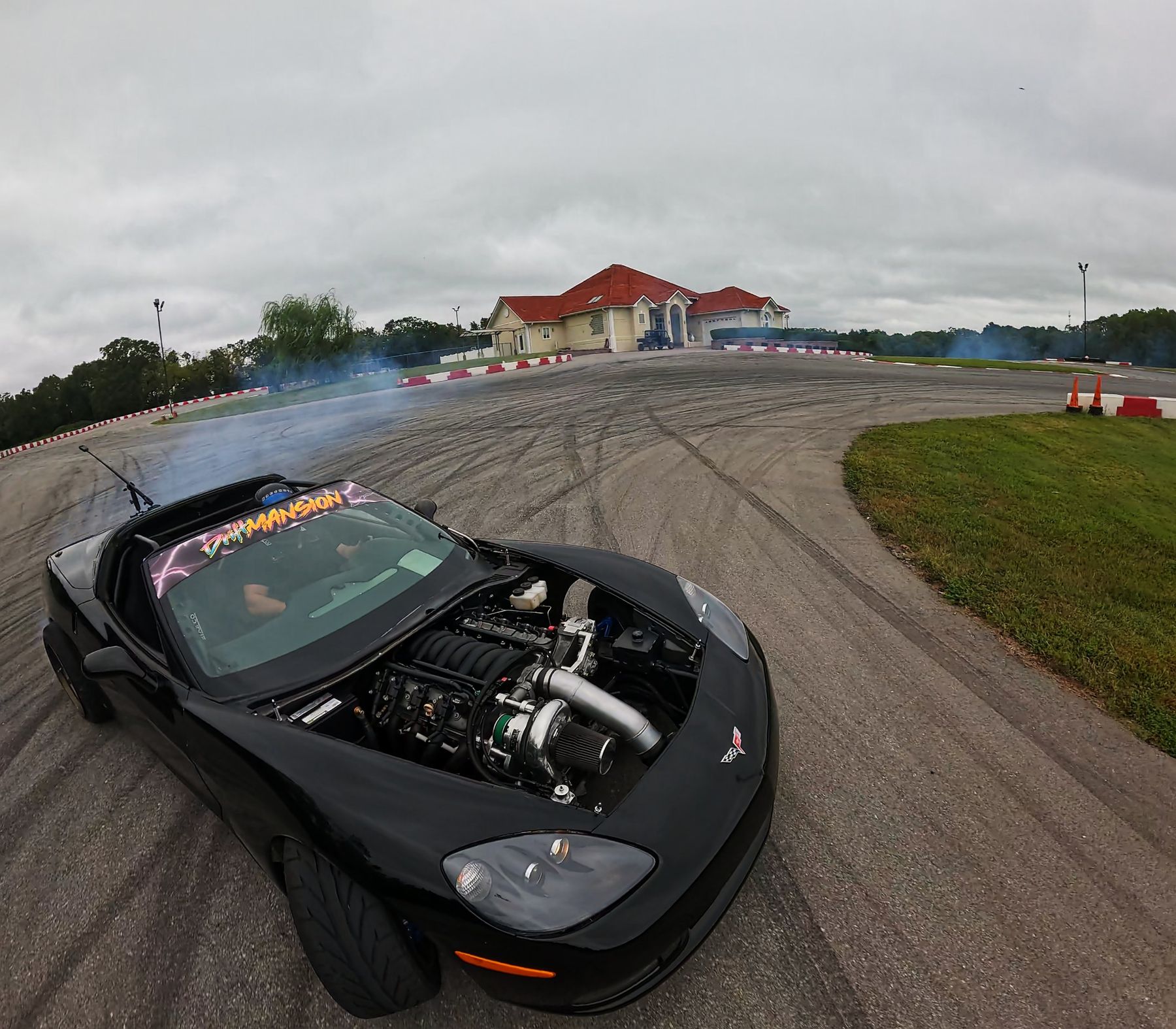 Wide-angle shot of a black Corvette with an exposed turbo engine drifting on a track